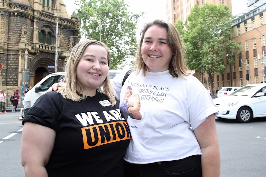 Kate and Nellie stand on the street wearing t-shirts bearing union slogans.