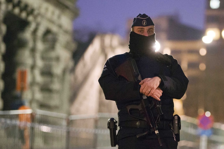 A police guard with half of his face covered stand outside a trial of Salah Abdeslam.