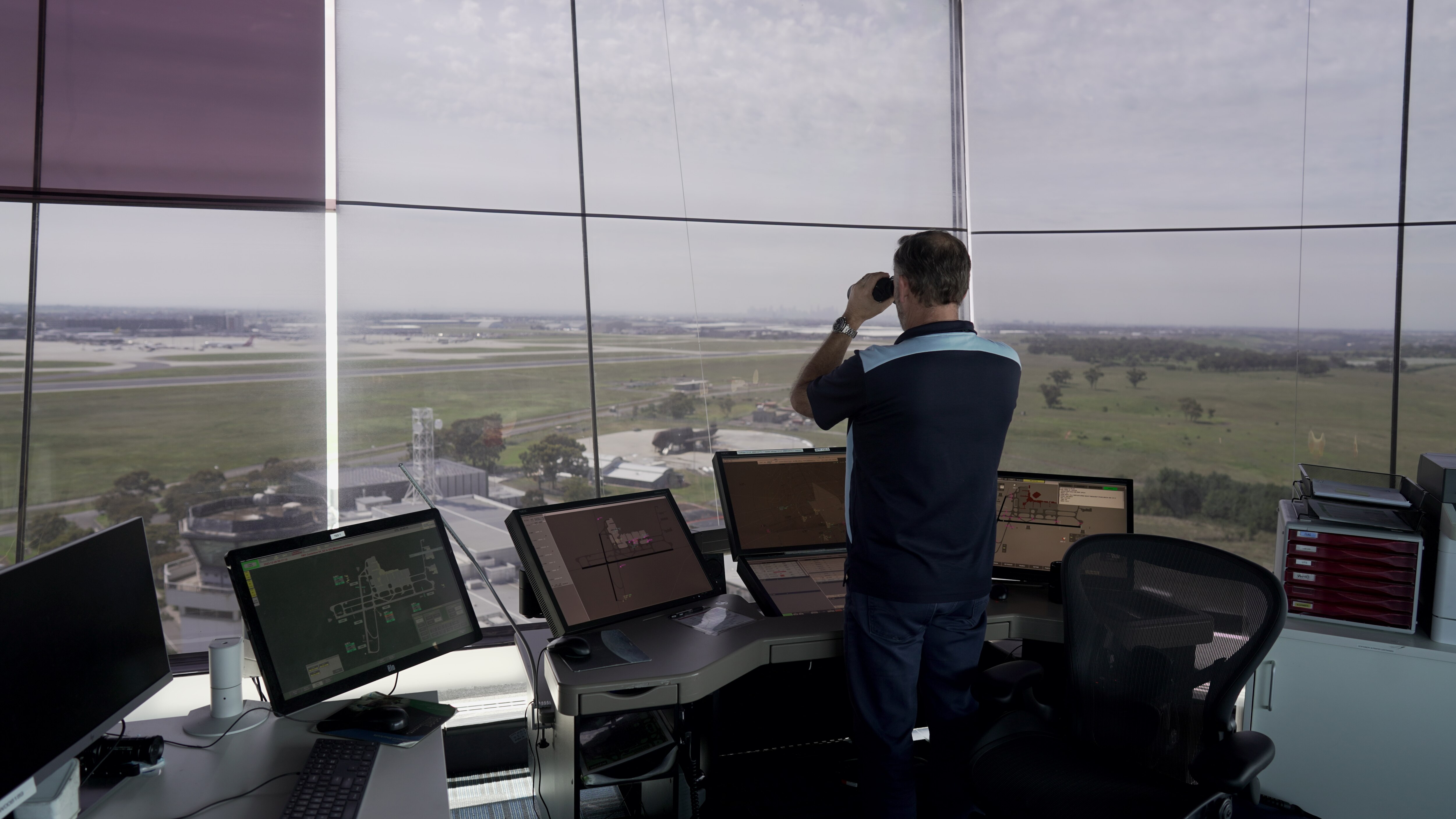Man looking through binoculars at an air traffic control tower.