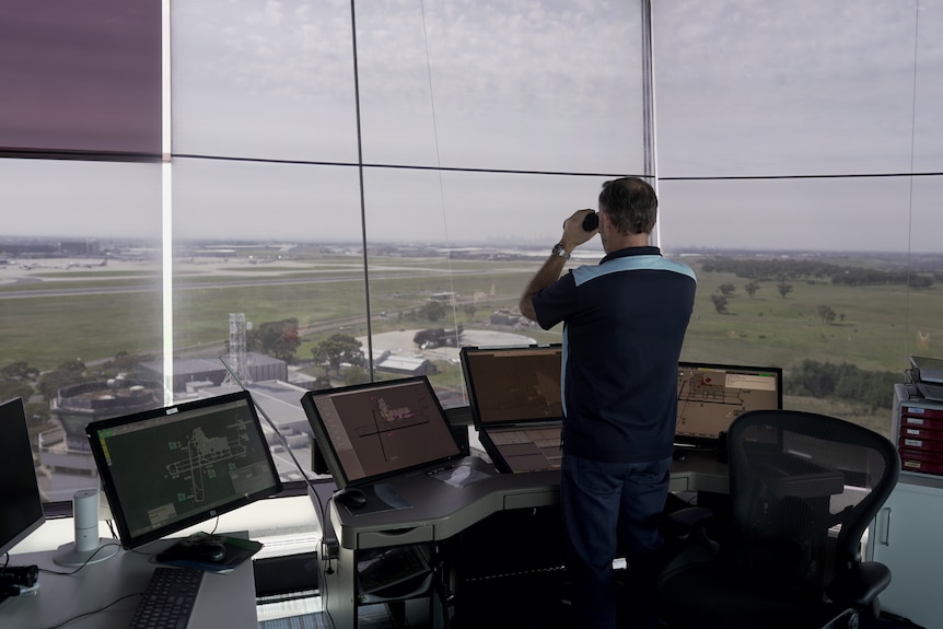 Man looking through binoculars at an air traffic control tower.