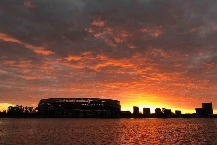A wide shot showing a glowing red sunrise over Perth Stadium and the surrounding skyline.