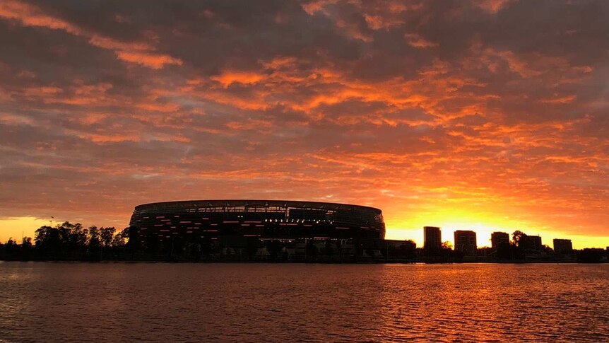 A wide shot showing a glowing red sunrise over Perth Stadium and the surrounding skyline.