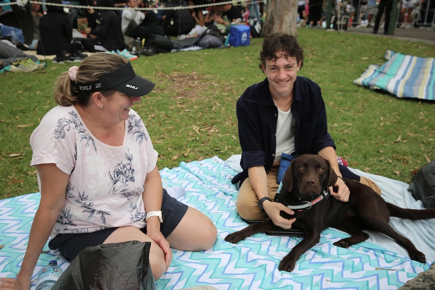 A mum and son smile and look at the camera, with the son petting his dog. 