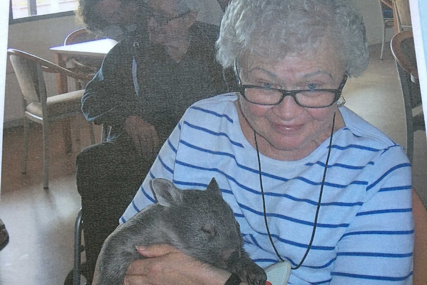 A woman with curly grey hair holding a juvenile wombat.