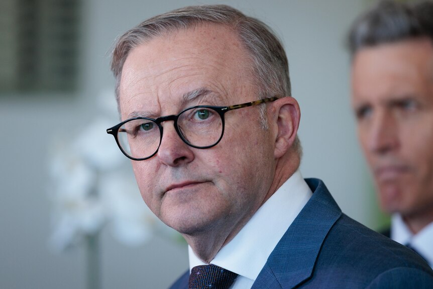 Anthony Albanese at a press conference, a close up of him in a pair of round glasses. 