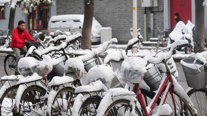 A cyclist rides past a row of snow-covered bicycles parked along a street in central Beijing