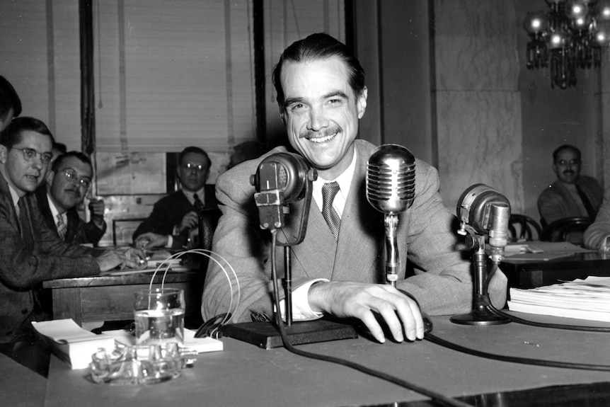 An old black and white photo of a man in a suit in front of an old style radio mic