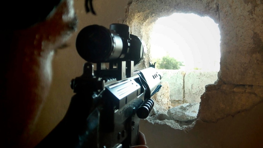 A member of the Free Syrian Army takes aim through a hole in a wall in a house in Homs.