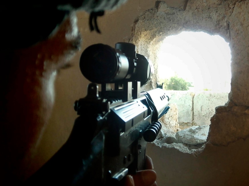 A member of the Free Syrian Army takes aim through a hole in a wall in a house in Homs.