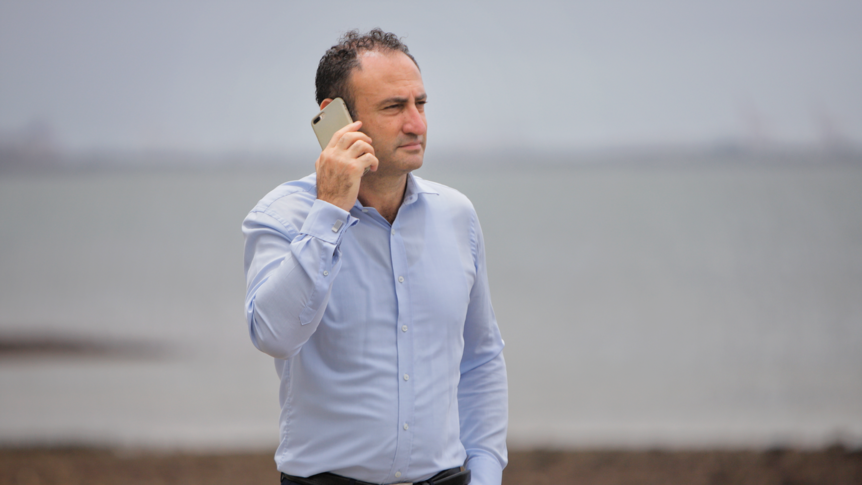 A man stand outside with a mobile phone held to his ear.