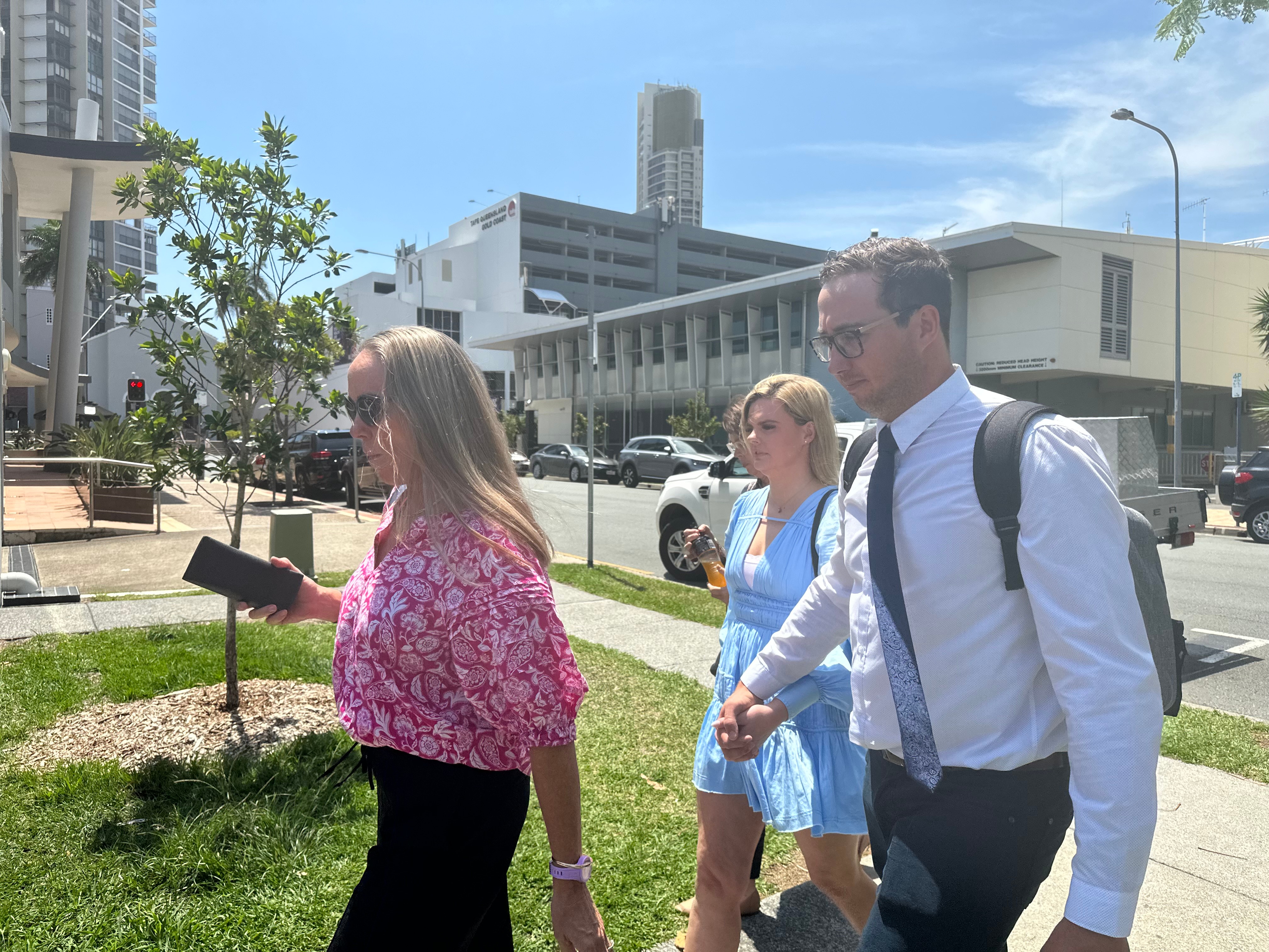 A man in a backpack holds hands with a woman while walking out of a courthouse