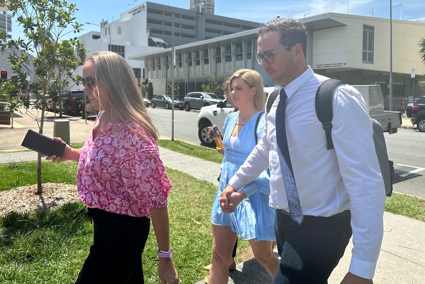 A man in a backpack holds hands with a woman while walking out of a courthouse