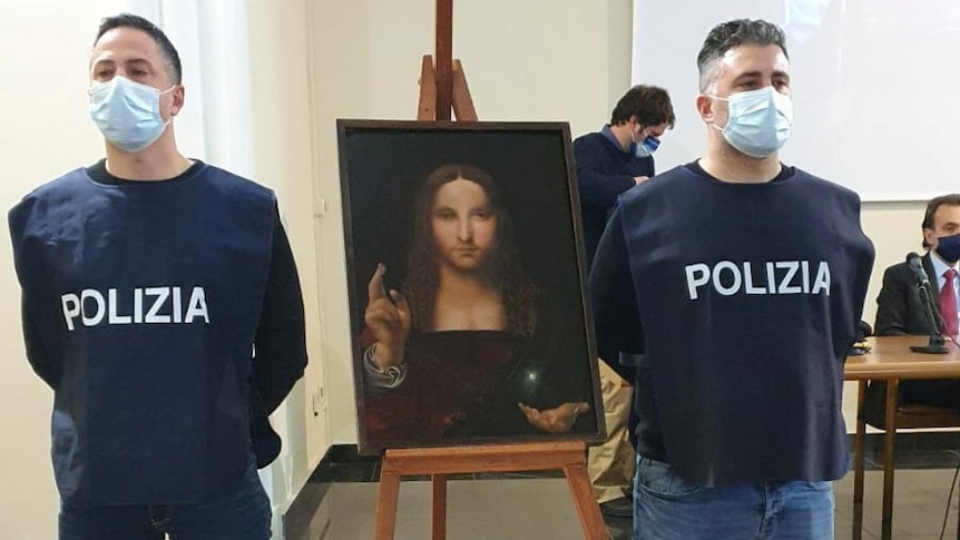 Police officers stand next to a recovered 500-year-old painting titled 'Salvator Mundi'.