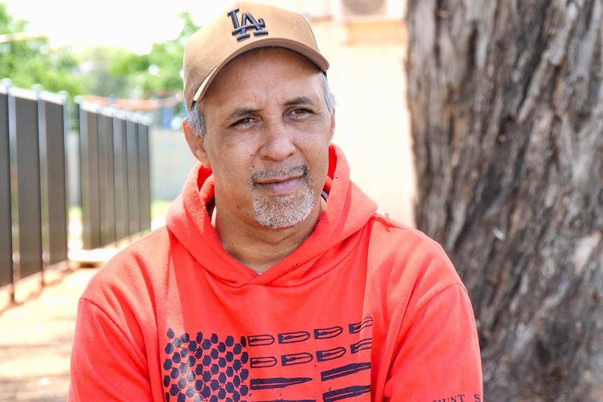 An aboriginal man wearing a light brown hat and a read hoodie in Wilcannia. 
