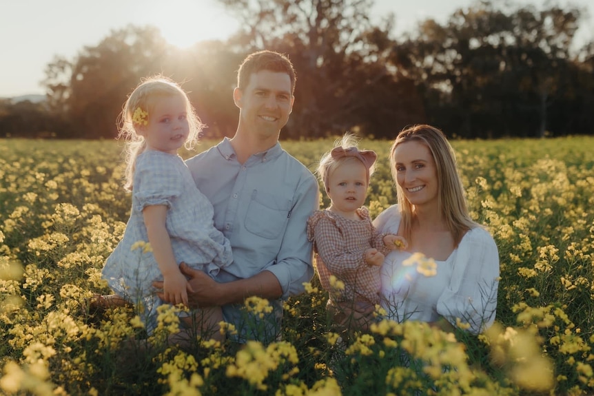 mum, dad and two small children photographed in a field of canola.