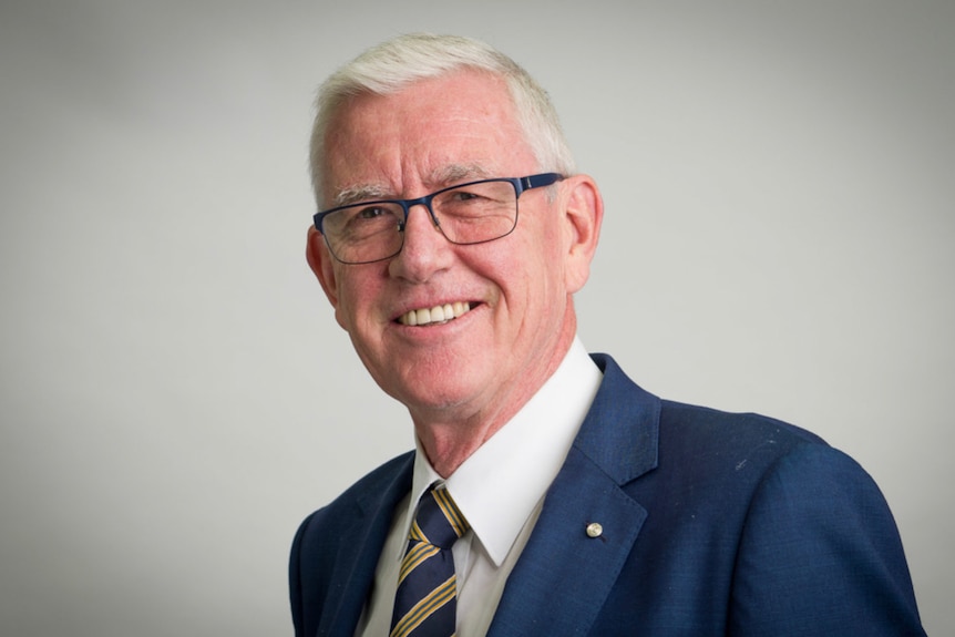 Man with grey hair and glasses wearing a suit. 