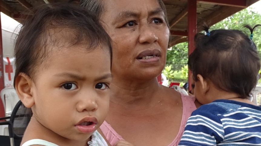 A woman holds two children in her arms at a medical shelter.