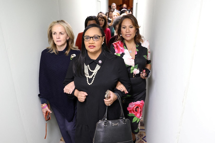 Women with arms linked march in narrow hallway.