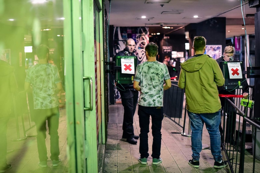 A photo taken from behind of a two men having their ID's scanned by bouncers at a Brisbane nightclub.