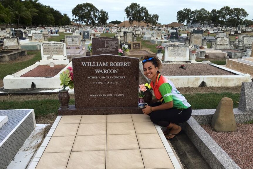Rachel Warcon kneels next to her great grandfather's grave with other graves in the background.