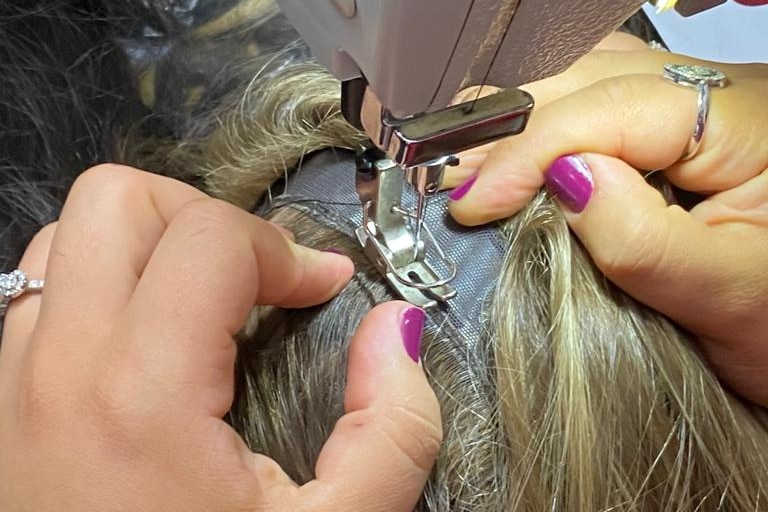Stitching human hair into a wig.