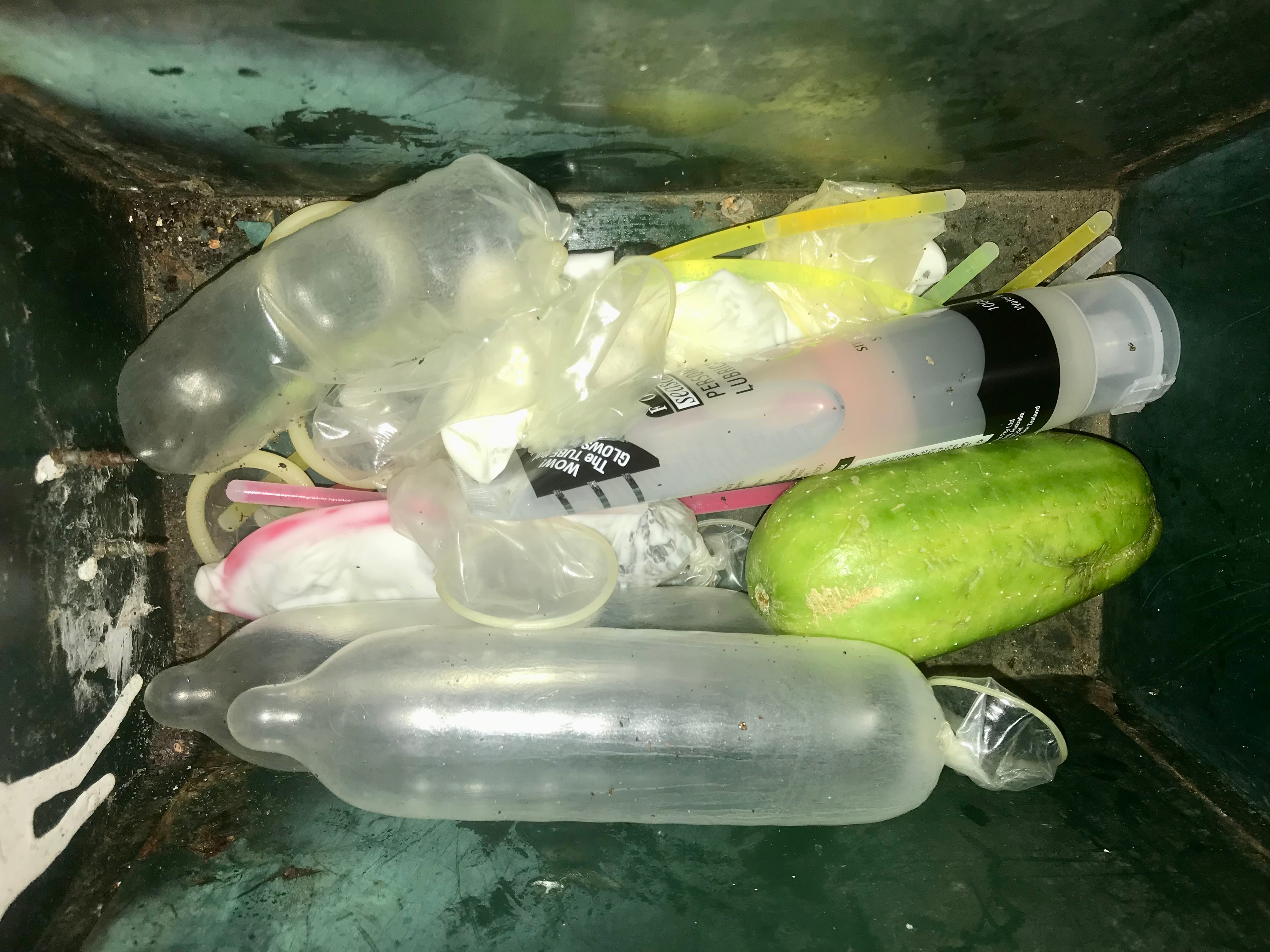 Close up of interior of a mailbox containing inflated condoms, glow sticks, lubricants and fruit.