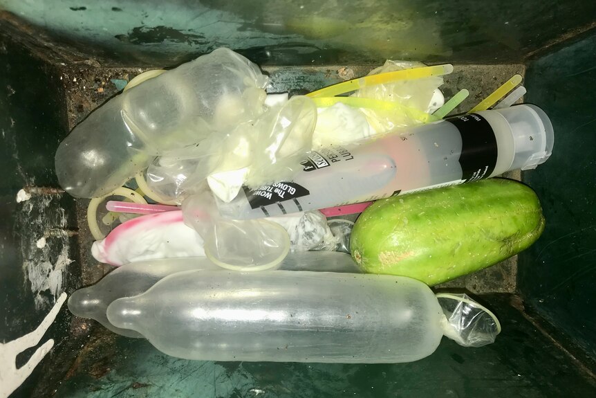 Close up of interior of a mailbox containing inflated condoms, glow sticks, lubricants and fruit.