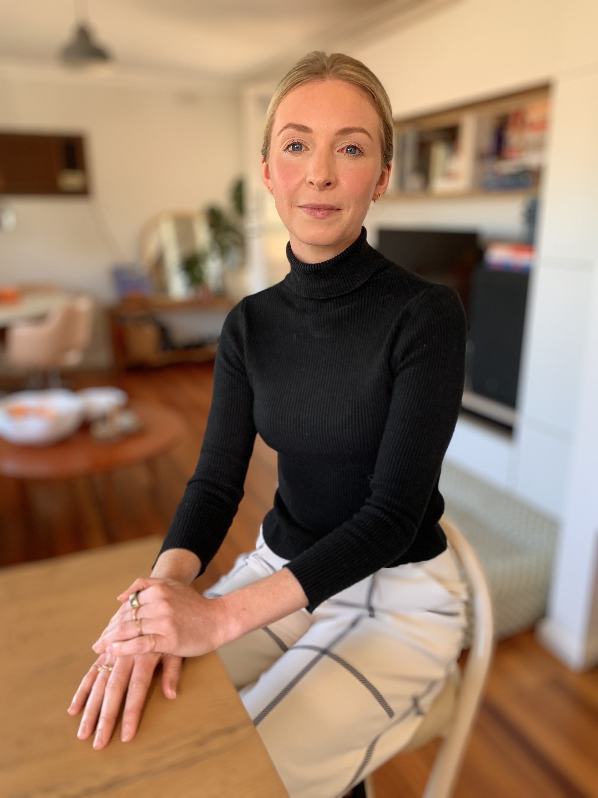 A woman with blonde hair and a black jumper looks at the camera with a neutral expression