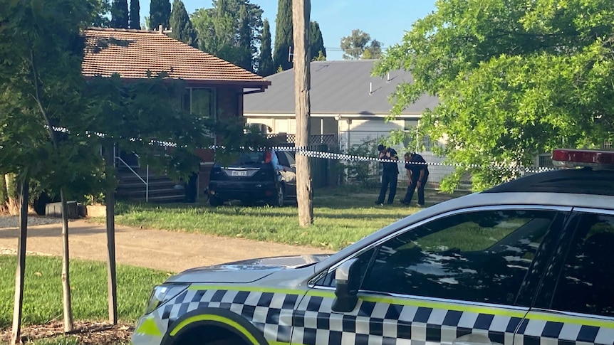 Police tape cordons off a home and car, as officers examine the crime scene.