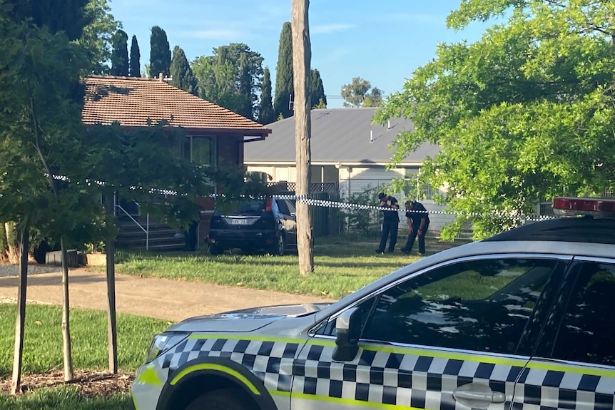 Police tape cordons off a home and car, as officers examine the crime scene.