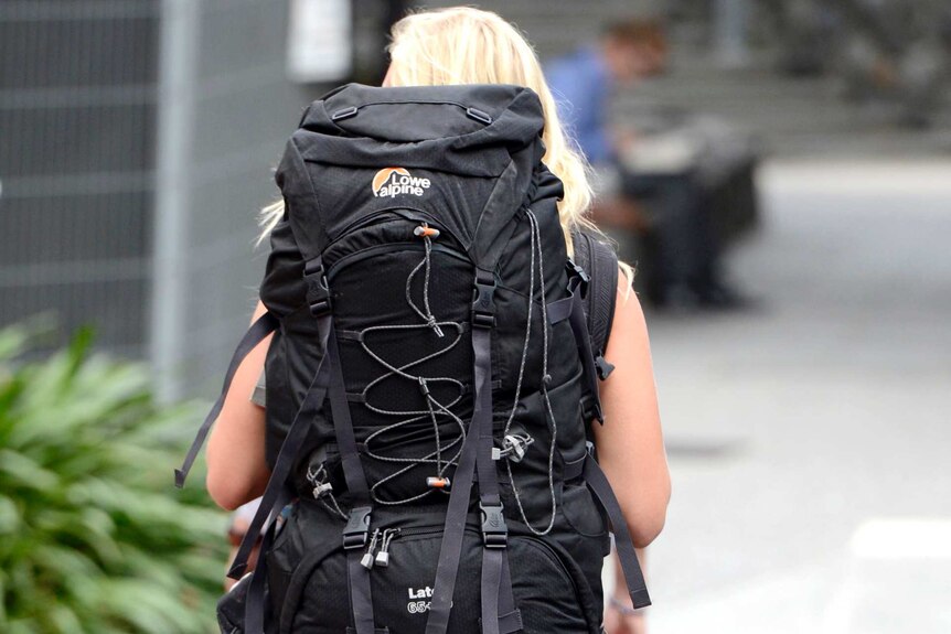 A blonde woman wearing a large backpack, as seen from behind.