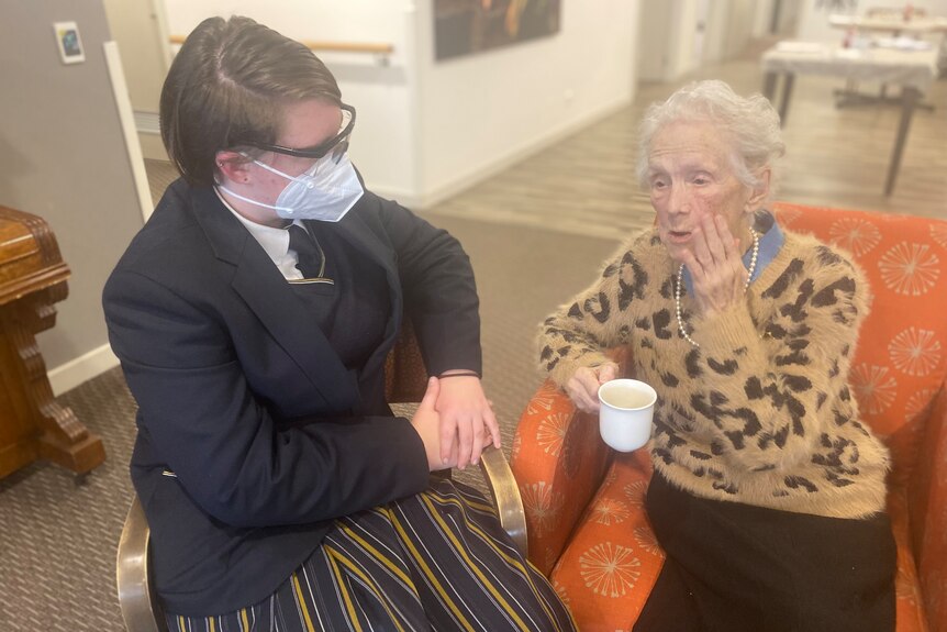 teenager and old woman sitting with a cup of tea, in conversation