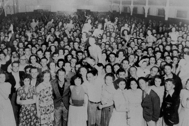 A black and white photo of a crowd in a dance hall.