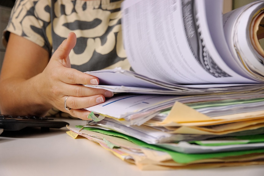 A woman's hands flick through a thick stack of paperwork. 