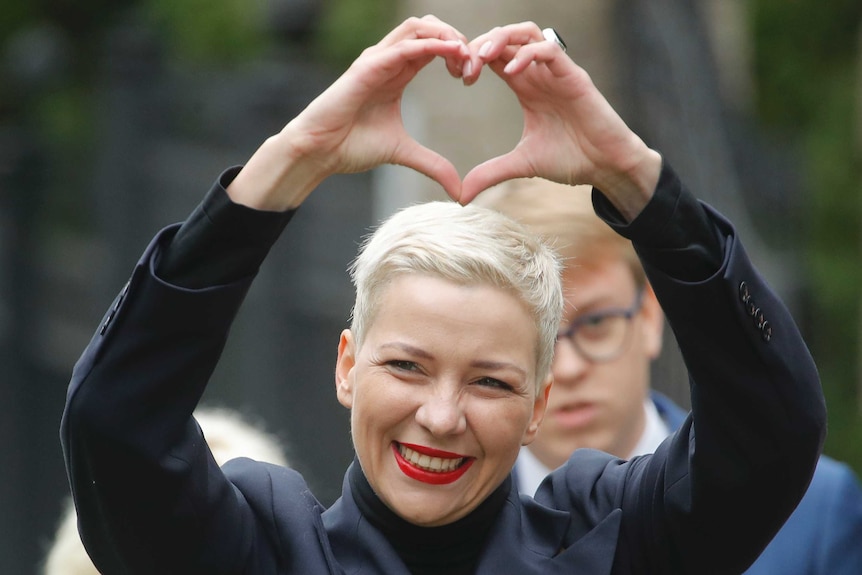 Maria Kolesnikova smiles as she makes a heart shape with her hands.