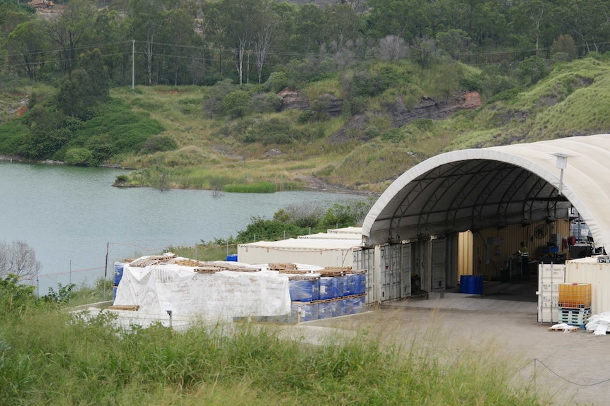 A large hanger style shed with shipping containers in front of a small lake