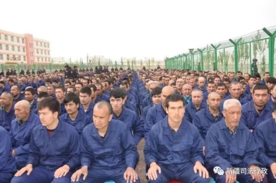 Lines of men sitting inside barbed wire wearing identical blue uniforms.