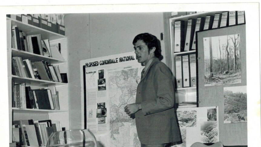 An archival photograph of Greg Roberts standing in front of a map saying proposed Conondale National Park.