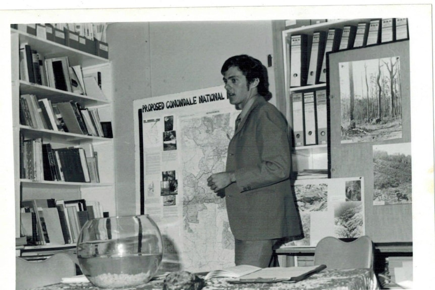 An archival photograph of Greg Roberts standing in front of a map saying proposed Conondale National Park.