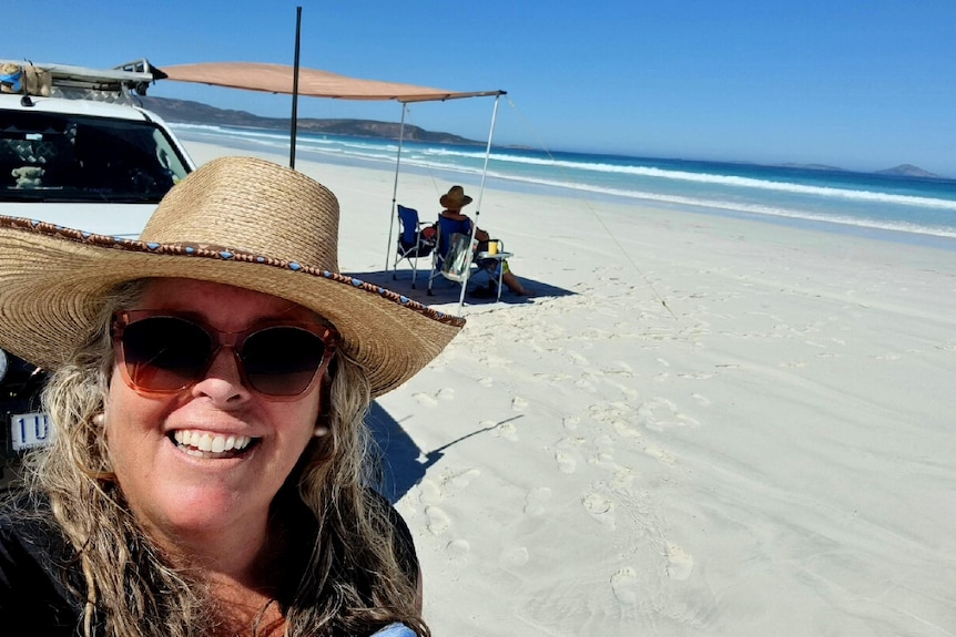 A woman in a straw hat close in shot with a man on a chair and beach in background