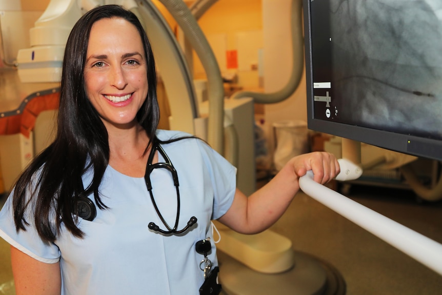 A woman wearing a stethoscope around her neck smiles.