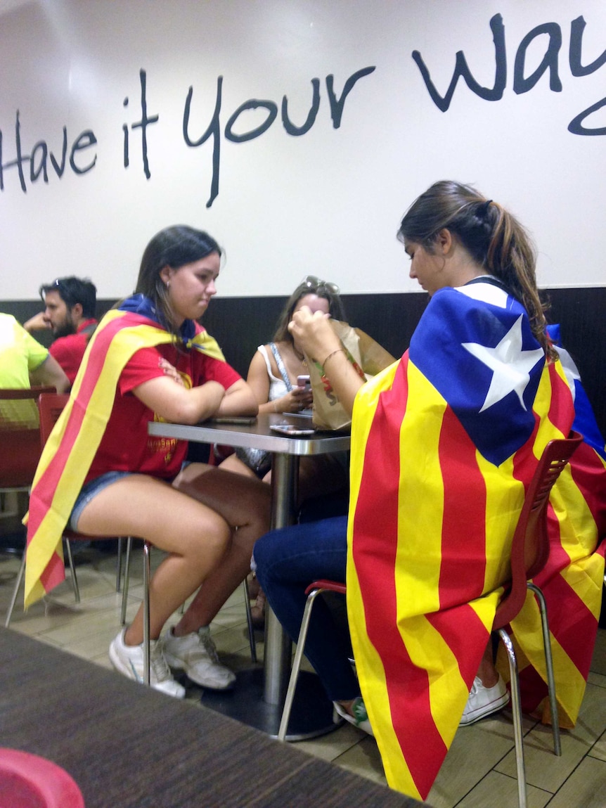 Two women draped in the red and white Catalan flag sit at a table.