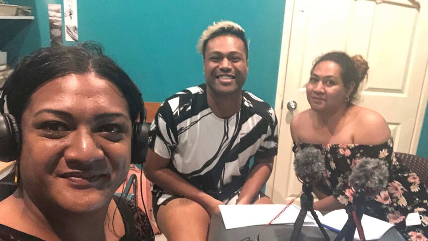 Three people smile for a selfie around an audio recording desk.
