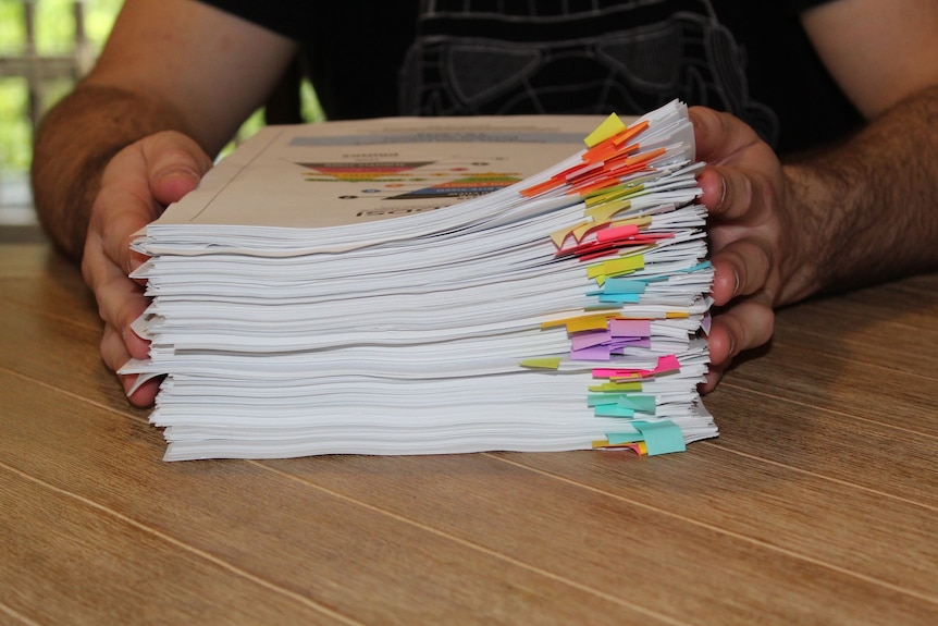 A large stack of papers on a table, with a person in the background.
