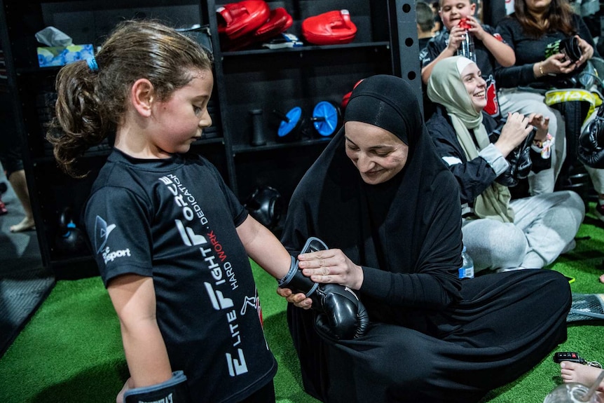 A mother helps her son put on his boxing gloves.