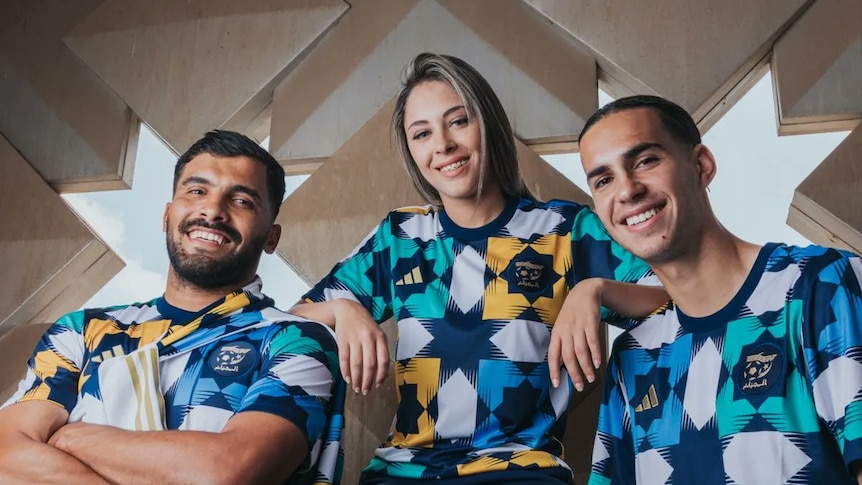 Three people smile at the camera wearing blue yellow and green shirts in geometric print.