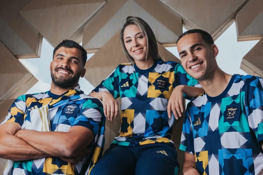 Three people smile at the camera wearing blue yellow and green shirts in geometric print.