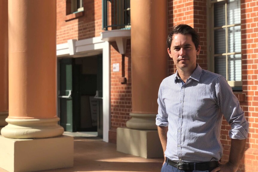 A man stands in a check shirt in front of the apricot coloured Maryborough City Hall.