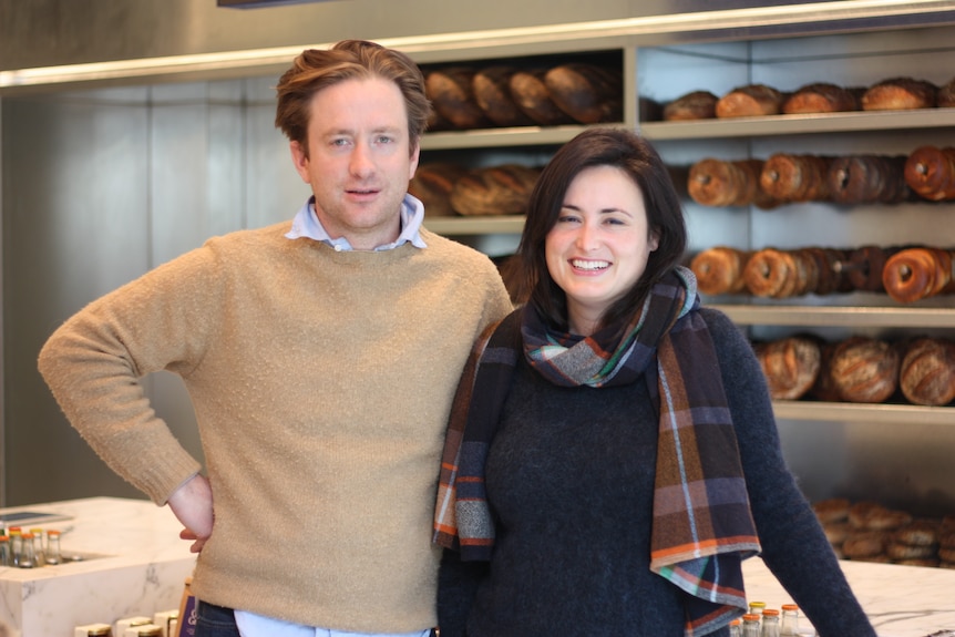 A man and a woman stand in front of dozens of loaves of bread