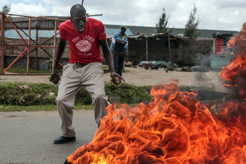 A man looks shocked and points at flames nearby.